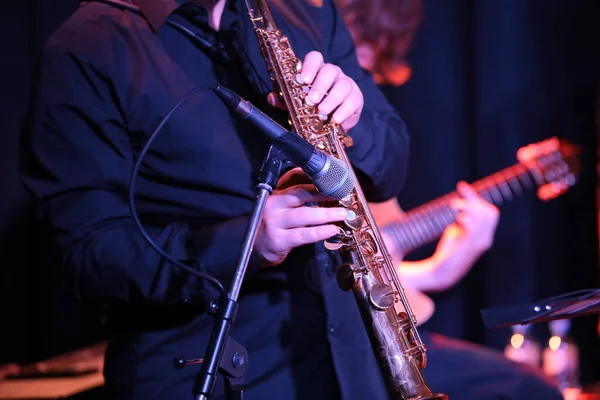 Musician playing a saxophone with a microphone close-up.Band of players performing on stage