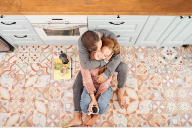 Evdeki mutfak zemininde oturmuş kahve içen genç ve güzel bir çiftin manzarası..