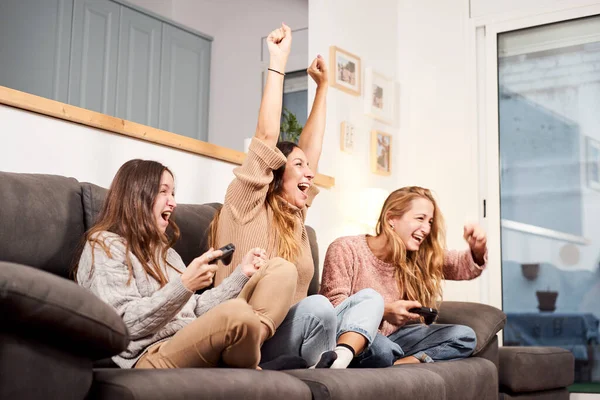Group of female friends sitting on sofa in living room and playing video games at home.