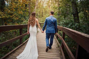 Ormanda bir köprü boyunca yürüyen yeni evli bir çiftin arka görüntüsü..