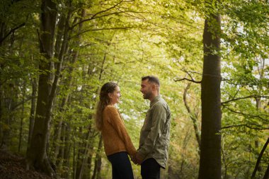 Mutlu genç çift el ele tutuşup, güzel bir sonbahar gününde ormanda birbirlerine bakıyorlar..