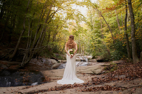 High angle rear view of beautiful young bride holding a bouquet on her back in the forest.