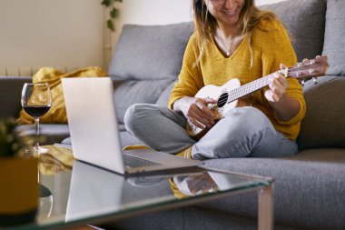 Gülümseyen kadın bilgisayarından ukulele çalmayı öğreniyor..