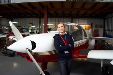 Genç bayan pilot hangarın içinde uçağının önünde gülümsüyor..