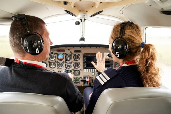 Pilot stajyer pilotun ve kokpitteki kadın uçuş eğitmeninin arka görüntüsü. O, onun açıklamalarıyla ilgilenen kadın eğitmenin yanında oturuyor..