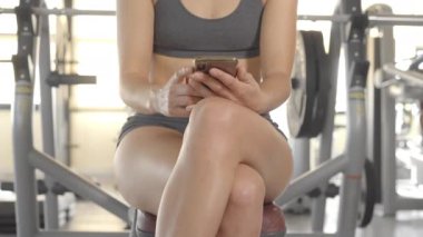 Spor giyim salonunda cep telefonu kullanan yüzsüz genç bayan sporcu. Yedek kulübesinde dinlenirken telefona bakıyor. Güzel fit kız akıllı telefonuyla mesajlaşıyor..