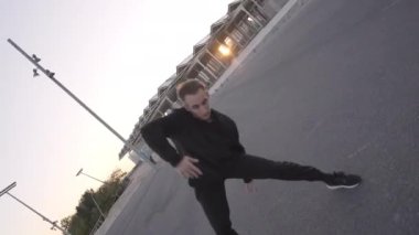 Siyah elbiseli atletik genç adam şehir ortamında çağdaş dans ediyor ve arka planda günbatımında takla atıyor..