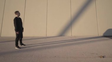 Şehir dışında egzersiz yaparken gri bir duvarın önünde çağdaş siyah dans eden atletik genç adam..