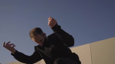 Şehirde akrobatik egzersizler yaparken şehir ortamında çağdaş dans eden siyah elbiseli atletik genç adam..