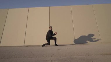 Gri bir duvarın önünde çağdaş siyah dans eden atletik genç adam şehirde akrobatik egzersizler yaparken takla atıyor..