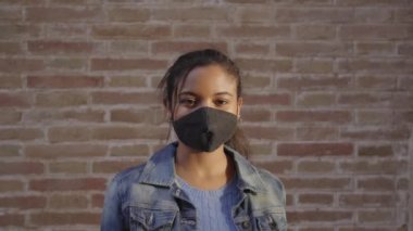 Dışarıdaki kameraya bakan yüz maskesi takan Afro-Amerikalı bir kadının portresi. Covid19 salgınından dolayı koronavirüs zamanlarında yeni bir normal..