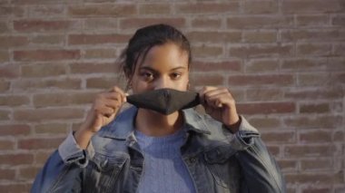 Açık havada maske takan ve kameraya bakan Afro-Amerikalı bir kadının portresi. Covid19 salgınından dolayı koronavirüs zamanlarında yeni bir normal..