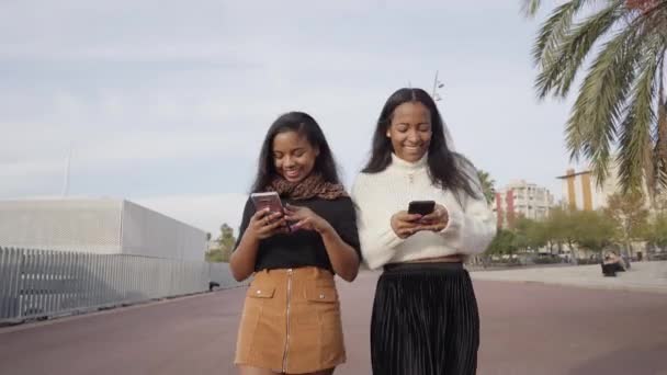 Δύο Μαύρα Κορίτσια Που Περπατούν Μια Πόλη Ενώ Χρησιμοποιούν Ένα — Αρχείο Βίντεο