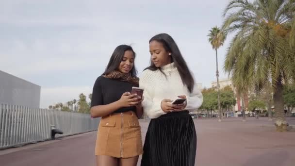 Két Fekete Lány Sétál Városban Miközben Mobiltelefont Használnak Nevetnek Emberek — Stock videók