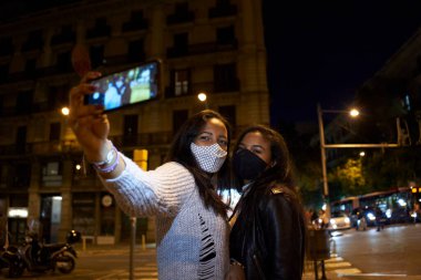 Yoğun bir şehirde, gece vakti selfie çeken iki zenci kadın arkadaş..