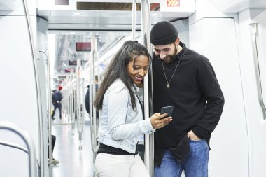 Metro vagonunda cep telefonlarını kullanan genç bir çiftin portresi. Toplu taşıma araçlarında internette bir şeylere danışmanlık yapıyorlar..