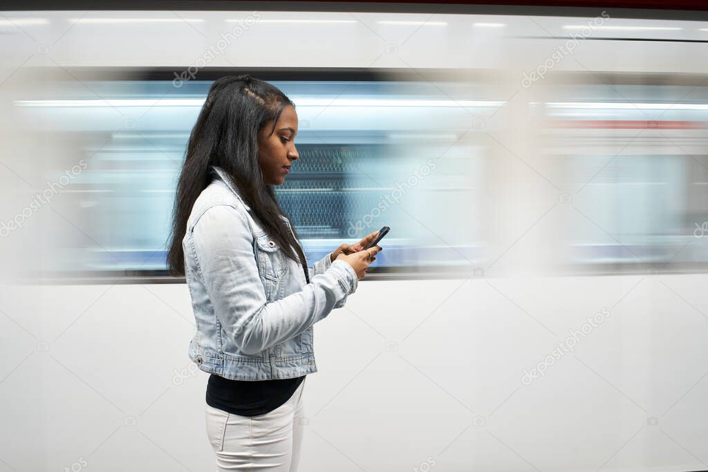 Portrait of a young woman with a mask using her mobile phone in the metro. The movement of the subway caravan in the background.