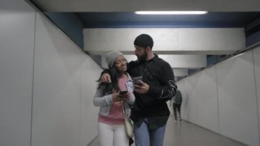 Bir metro koridorunda birbirine sarılan ırklar arası genç bir çift. Genç siyahi bir kadın ve genç bir Kafkasyalı akıllı telefonundan bir şeyler konuşuyorlar..