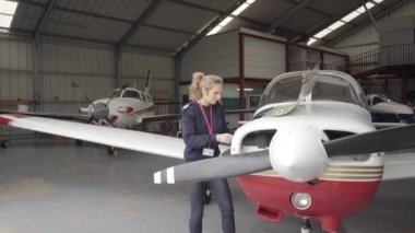 Hangardaki kadın pilot bir uçağın motorunda bakım yapıyor, yağ seviyesini kontrol ediyor. Uçuş öncesi hazırlıklar.