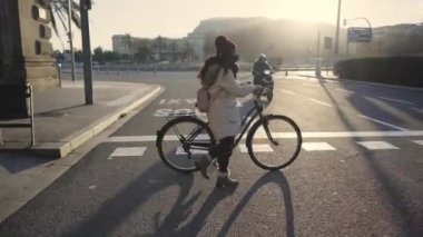 Kışın giyinmiş siyah bir kadın gün batımında şehirde bir bisikletle kalabalığın içinden geçiyor..