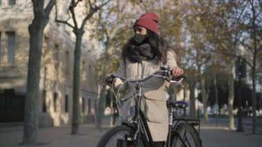 Kışları giyinmiş siyah bir kadın gün batımında bir şehirde bisikletle dikiliyor. Bir telefon alır, konuşur ve güler..