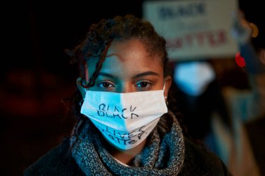 An intense look from an African-American woman demonstrating against racism. Demonstrators in a city with banners fighting for their rights, holding signs. Black Lives Matter. clipart
