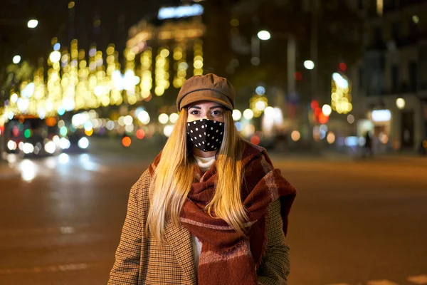 一个年轻的金发女人 戴着面具 面对着摄像机 在一个城市的夜晚 有很多的背灯和汽车经过的合影 冬季气氛 — 图库照片