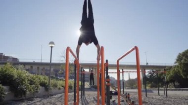 Bir adamın tek eliyle dengede durması, halter parkında amuda kalkması. Açık hava egzersizi. Sağlıklı yaşam, spor, eğitim, beden eğitimi kavramı.