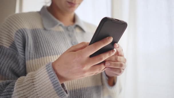 使用电话 上网或与应用程序互动的女人 站在窗边用智能手机的女人 前视镜拍摄 待在家里 — 图库视频影像
