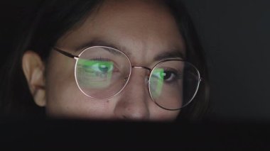 Bilgisayarda çalışan bir kadının gözlerini kapatıyoruz. Bilgisayar ekranı gözlüklere yansıyor.