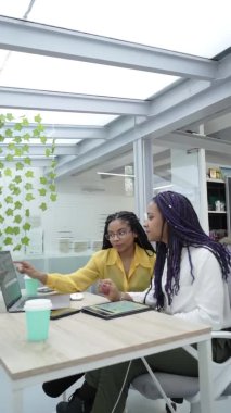 Genç siyahi kadınların çeşitli elektronik cihazlarda analitik verileri incelerken dikey çekimleri. Milenyum işçileri için bir ofiste çalışıyorum..