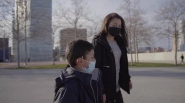 Bir çocuğun gün batımında annesiyle birlikte şehirde ağır çekimde yürümesi. Kendilerini bir maskeyle koronavirüsten korurlar..