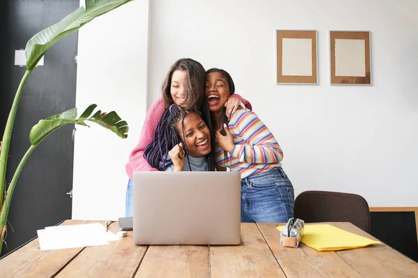 Un grupo de mujeres abrazándose eufóricamente celebran la buena noticia frente a la computadora. Exitoso grupo multiétnico emocionado y feliz. — Foto de Stock