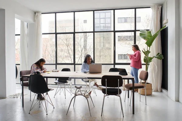 En la oficina. Tres empresarias trabajan juntas sin máscaras, manteniendo una distancia segura. Dos de ellos están trabajando en el escritorio y uno está charlando en su teléfono inteligente cerca de la ventana. — Foto de Stock