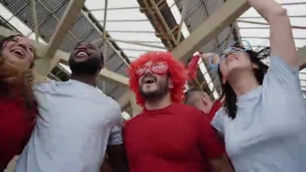 Grupp människor firar tillsammans hoppar och kramas medan hejar på sitt idrottslag från en stadion. Jublande fans titta på matchen i kostym på stadion. — Stockvideo