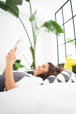 Genç bir kadın rahat bir odada kitap okuyor, sayfayı çeviriyor, öğreniyor, çalışıyor, eğitim alıyor, kitap okuyor, evde kalıp dinleniyor..