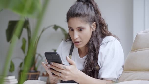 Hermosa joven escuchando usando un teléfono celular en casa. Mujer divertida y feliz recibe buenas noticias en su teléfono inteligente, feliz celebra las buenas noticias. Tener suerte. — Vídeos de Stock