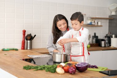 Mother teaches her son to cook some vegetables in the kitchen. Lifestyle with latin people. Child learning to cook.