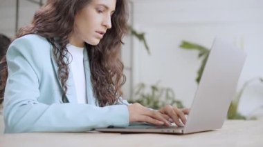 Close up of beautiful young business woman typing on laptop keyboard. Female office worker in formal suit works concentrated in modern office in slow motion.