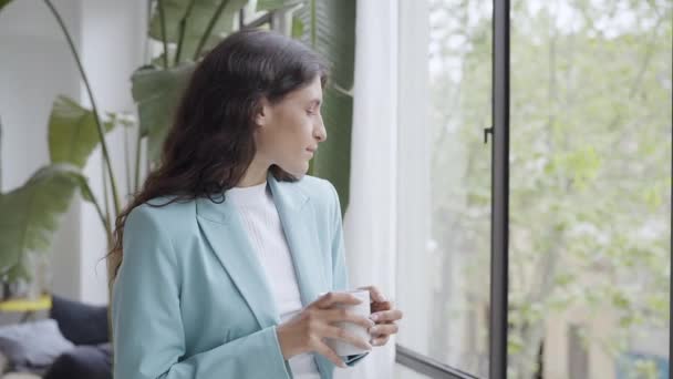 Young business woman enjoying relaxing with her morning coffee or tea, looking out the window. Beautiful latina woman getting inspired on break from work at the office. — Stock Video