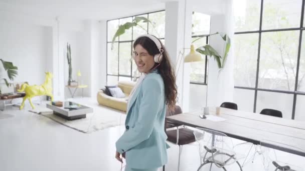 Jonge zakenvrouw danst in het kantoor, vrolijk en blij voor haar werk goed gedaan, kijkend naar de camera glimlacht en knipoogt ze terwijl ze danst. Latijnse vrouw viert successen in de pauze van het werk. — Stockvideo