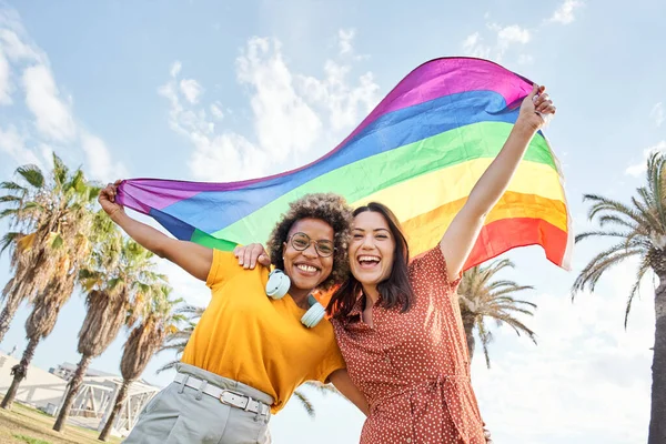 Genç lezbiyen çift gurur gününü gökkuşağı bayrağıyla kameraya bakarak kutluyor. Homoseksüellik kavramı, gay.