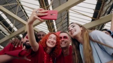 Bir grup taraftar stadyumdan spor takımı için tezahürat yaparken selfie çekiyorlar. Neşeli erkek ve kadın taraftarlar stadyumda maç izlerken telefonlarıyla video kaydediyorlar..