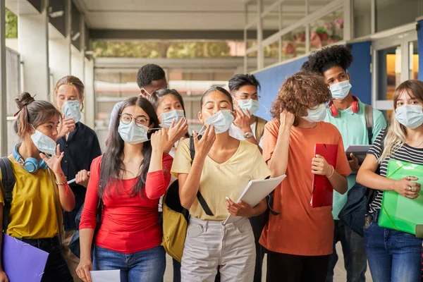 Bir grup öğrenci maskelerini takıyor ya da çıkarıyor. Çeşitli etnik kökenlere sahip gençler covid virüse karşı güvenlik önlemleri alıyorlar. Okula geri dön..