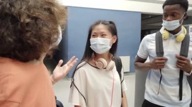 Koronavirüs salgınından korunmak için maske takan genç öğrencilere sınıfa geri dönüyoruz. Gençler lisenin koridorlarında konuşuyorlar..
