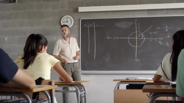 El profesor en el aula enseña matemáticas y geometría a los estudiantes. Escribe con tiza en la pizarra. — Vídeo de stock