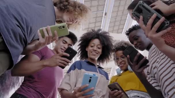 Vista de bajo ángulo de un grupo de jóvenes adolescentes sosteniendo teléfonos celulares. Rostros sorprendidos mirando la pantalla. Concepto de tecnología, conexión, colorido. — Vídeo de stock