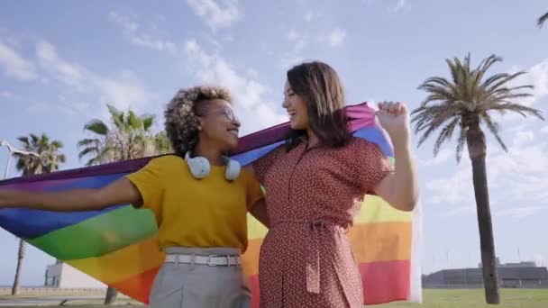 Jovem casal lésbico abraçando e celebra o dia do orgulho com bandeira do arco-íris. Conceito de homossexualidade, gay. Movimento lento. — Vídeo de Stock