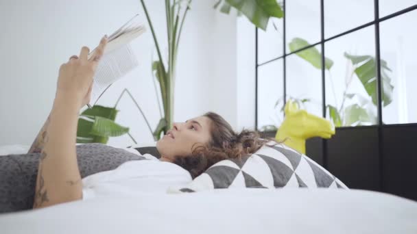 Young woman reading a book in the cozy room, turning the page, learning, studying, education, reading books, concept of staying at home and relaxing. — Stock Video