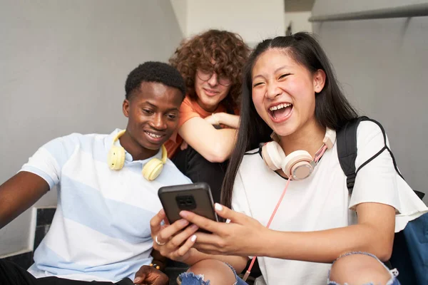 Grupo de adolescentes estudantes de diferentes etnias que utilizam telefones celulares. Menina chinesa olhando para a câmera enquanto ri. — Fotografia de Stock